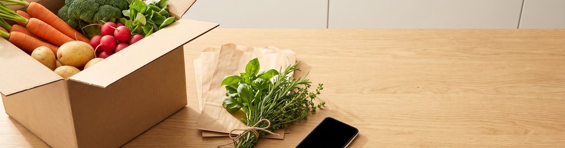 Kochbox-Karton mit frischem Gemüse, Smartphone und Schlüssel auf einer Küchenarbeitsplatte