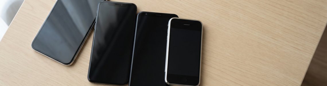 Fünf Smartphones verschiedener Generationen mit ausgeschalteten Displays nebeneinander auf einem Holztisch