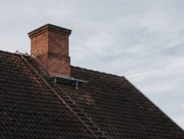 Gemauerter Ziegelschornstein mit Steigleiter auf einem Ziegeldach vor grauem Winterhimmel