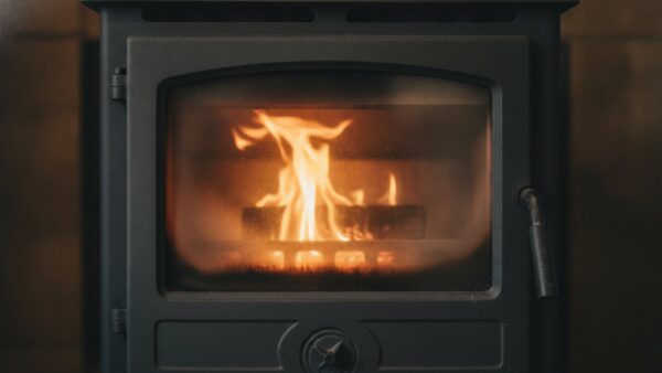 kaminofen 2026 bild 3 Teilweise verrußte Sichtscheibe eines Kaminofens mit kleinem Holzfeuer dahinter