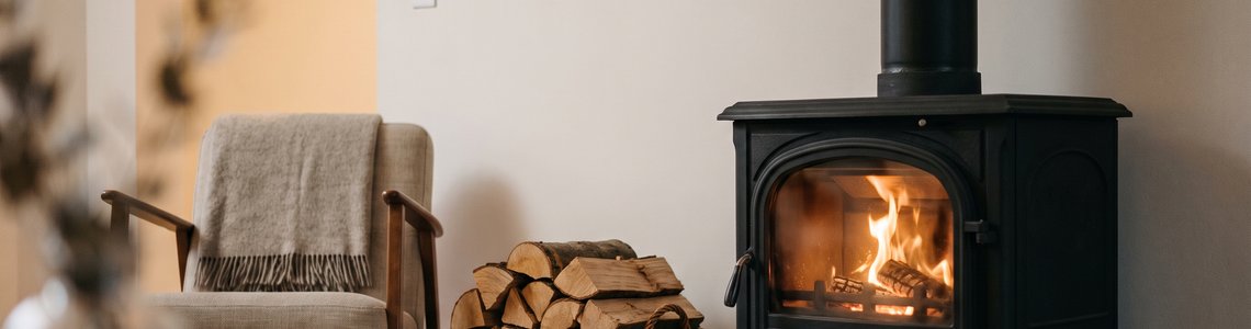 Schwarzer Kaminofen mit klarer Sichtscheibe und Holzkorb in einem hellen Wohnzimmer