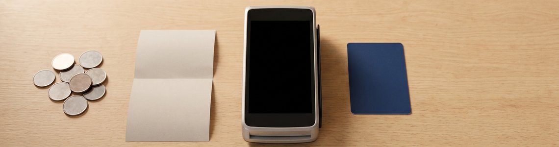 Münzen, Papierschein, Kartenterminal und unbedruckte Karte auf einem Café-Tresen