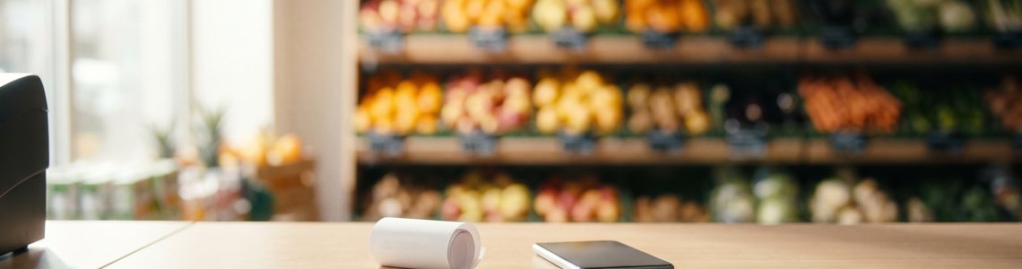 Kassentresen mit eingerollter Papierrolle und Smartphone vor unscharfen Obstregalen