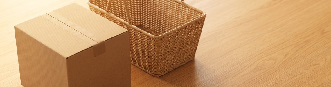 Unbedruckter Versandkarton und leerer Einkaufskorb auf hellem Holz