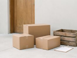 Drei unbedruckte Versandkartons vor einer hellen Hauswand mit geschlossener Tür