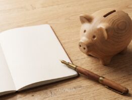 Sparschwein neben aufgeschlagenem Notizbuch und Füller