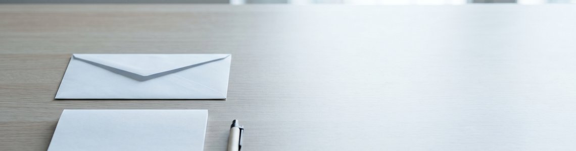 Leerer Büroschreibtisch mit unbedrucktem Briefumschlag, Notizblock und Stift