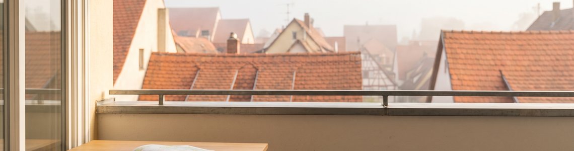 Blick von einem Altbau-Balkon über die Ziegeldächer einer europäischen Altstadt im Morgendunst