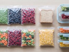 Flach gepackte Gefrierbeutel und Dosen mit Erbsen, Beeren, Brot und Gemüse auf einer Arbeitsplatte