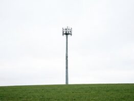 Schlanker Mobilfunkmast vor hellem bewölktem Himmel