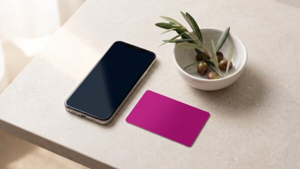 magenta pay bild 1 Smartphone neben einer unbedruckten magentafarbenen Karte und einem Olivenzweig auf heller Steinplatte