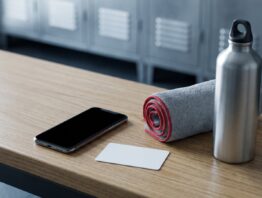 Smartphone, unbedruckte Karte, Handtuch und Trinkflasche auf einer Umkleidebank – McFit Vertrag mit der App verbinden