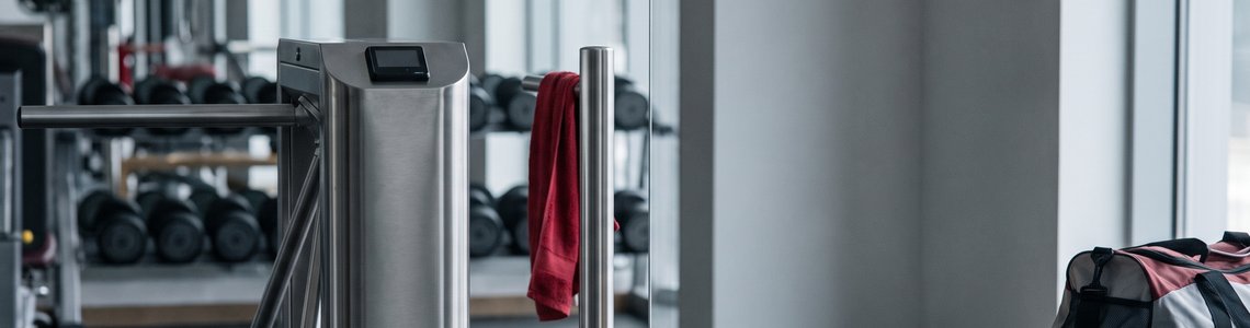 Eingangsbereich eines Fitnessstudios mit Drehkreuz, Kartenleser und Smartphone auf einer Bank – McFit Login
