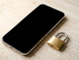 Smartphone mit dunklem Bildschirm neben einem kleinen Vorhängeschloss