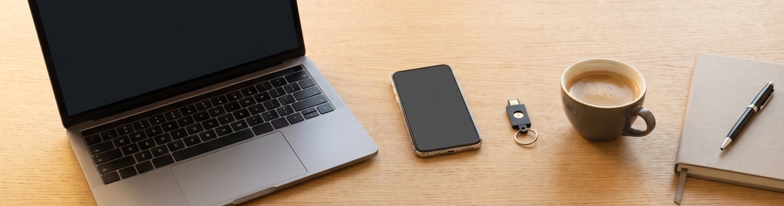 Notebook, Smartphone und Sicherheitsschlüssel auf einem hellen Holzschreibtisch