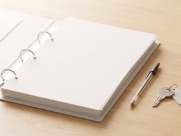 Aufgeschlagener Aktenordner mit leeren Blättern, Kugelschreiber und Wohnungsschlüssel auf einem Holztisch