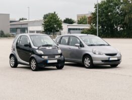 Winziges Kleinstfahrzeug im Größenvergleich neben einem Kompaktwagen auf leerem Asphalt