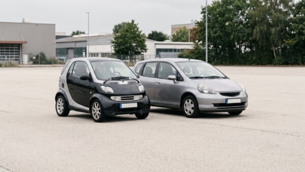 mopedauto kaufen bild 1 Winziges Kleinstfahrzeug im Größenvergleich neben einem Kompaktwagen auf leerem Asphalt