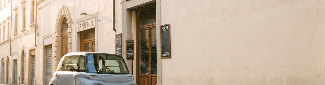 Kleines zweisitziges Elektro-Kleinstfahrzeug am Rand einer sonnigen Altstadtgasse