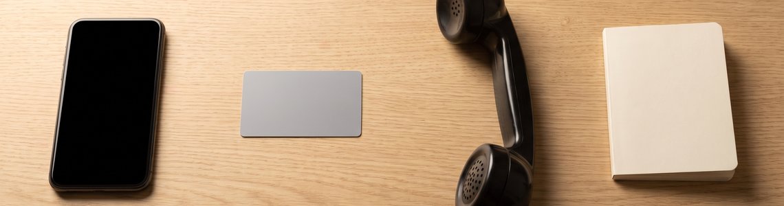 Smartphone, unbedruckte Bezahlkarte und abgenommener Telefonhörer auf einem Holzschreibtisch