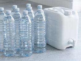 Unbeschriftete Wasserflaschen und ein weißer Kanister mit Zapfhahn auf hellem Steinboden