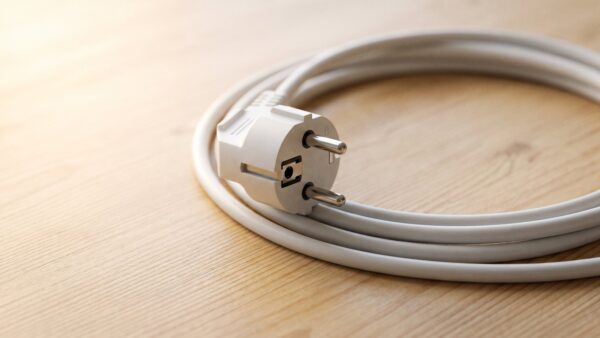 paketweiterleitung bild 3 Weißer Netzstecker mit aufgerolltem Kabel auf Holzfläche