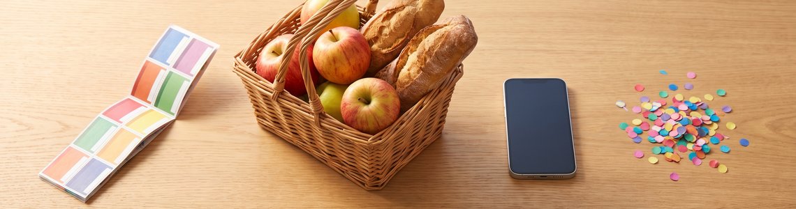 Couponheft, Einkaufskorb mit Äpfeln und Brot, Smartphone und Konfetti auf einem Holzschreibtisch