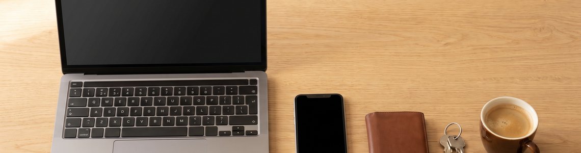 Notebook, Smartphone, Lederportemonnaie und Schlüsselbund auf einem hellen Holzschreibtisch