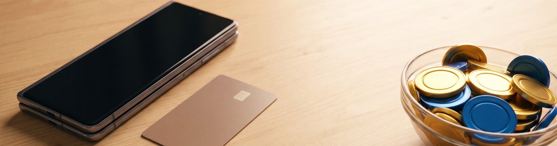 Smartphone mit dunklem Bildschirm, neutrale Bezahlkarte und eine Schale mit blauen und goldenen Spielmarken