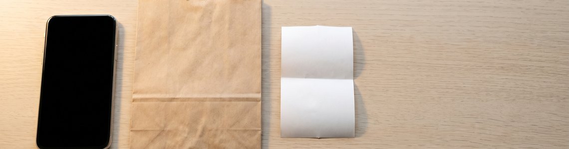 Smartphone, Papiertuete und leerer Kassenbon auf heller Holzfläche