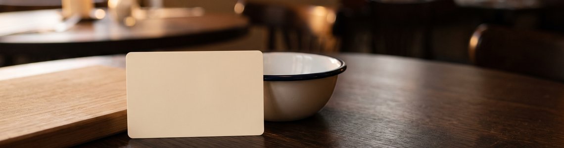 Unbedruckte Gutscheinkarte und Holzbrett auf dunklem Bistrotisch