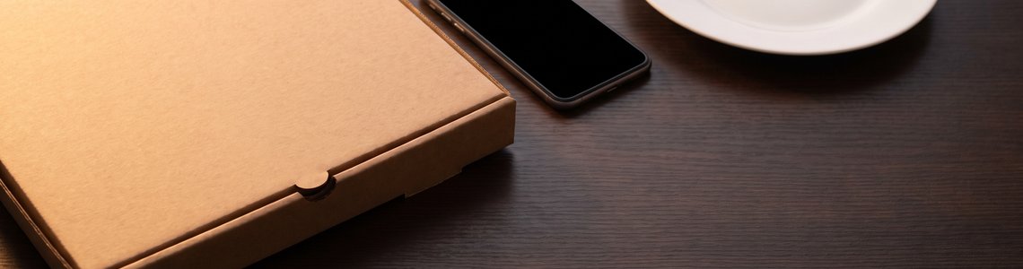 Unbedruckter Pizzakarton, Smartphone und leerer Teller auf dunklem Holz