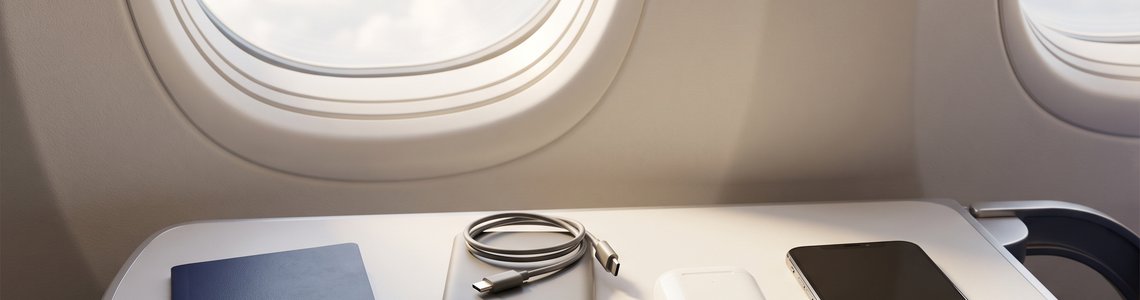 Powerbank, Smartphone, Ohrhörer und Reisepass auf dem Klapptisch am Flugzeugfenster