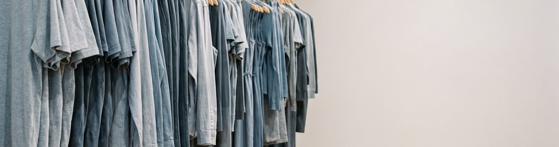 Lange Kleiderstange mit schlichten Kleidungsstücken in einem hellen Modegeschäft