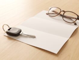 Autoschlüssel, leerer Briefbogen und Lesebrille auf hellem Holztisch