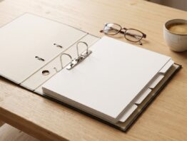 Geöffneter Aktenordner mit leeren Blättern, Lesebrille und Kaffeetasse auf Holztisch
