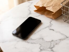 Smartphone mit schwarzem Bildschirm neben Papiertuete und Einkaufskorb