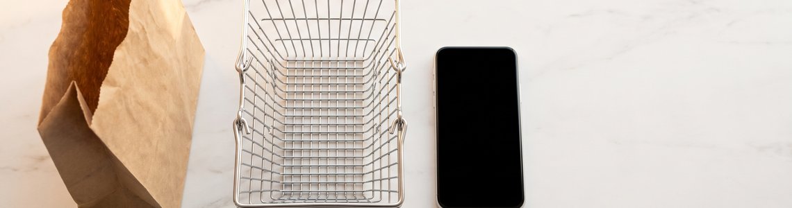 Leere Papiertuete, Drahtkorb und Smartphone auf heller Fläche