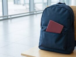 Geschlossener Rucksack auf einer Bank in einer Wartehalle, aus der Vordertasche schaut ein Reisepass