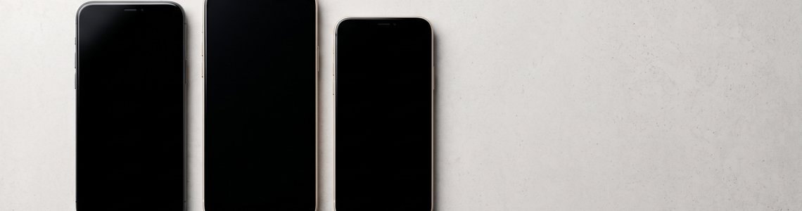 Drei moderne Smartphones in unterschiedlicher Größe nebeneinander auf heller Betonfläche