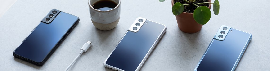 Drei moderne Android-Smartphones in verschiedenen Farben auf einem hellen Steintisch