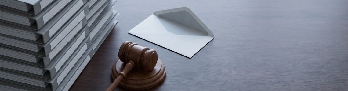 Unbeschriftete Aktenordner, Richterhammer und leerer Briefumschlag auf dunklem Schreibtisch