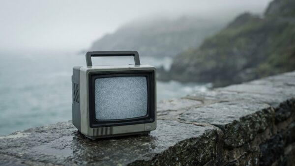 silent hill townfall bild 1 Alter tragbarer Röhrenfernseher mit Bildrauschen auf einer nassen Steinmauer vor nebliger Küste