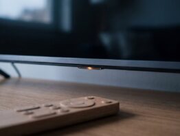 Nahaufnahme der Unterkante eines Fernsehers mit leuchtendem Statuspunkt und Fernbedienung