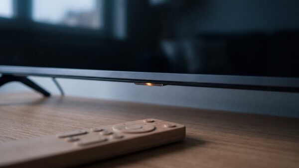 smart tv datenschutz bild 1 Nahaufnahme der Unterkante eines Fernsehers mit leuchtendem Statuspunkt und Fernbedienung