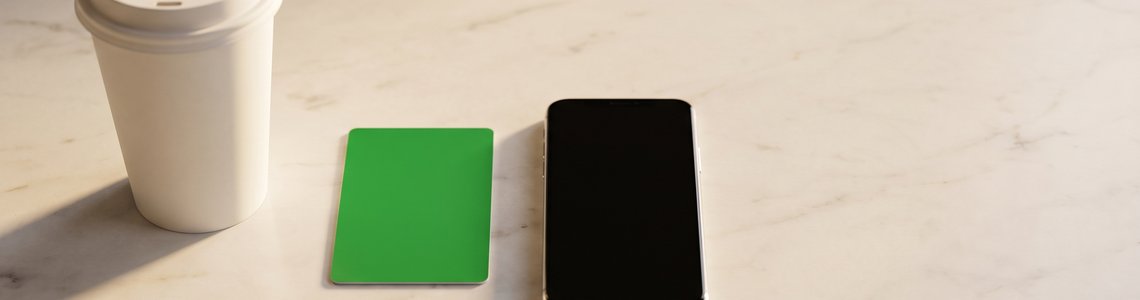 Unbedruckter Kaffeebecher, grüne Karte und Smartphone auf heller Theke
