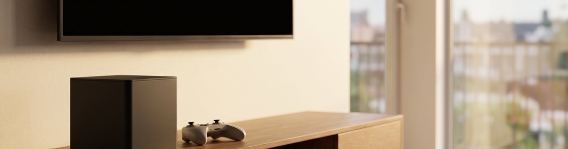 Kleiner schwarzer Würfel-PC auf einem Sideboard unter einem ausgeschalteten Fernseher