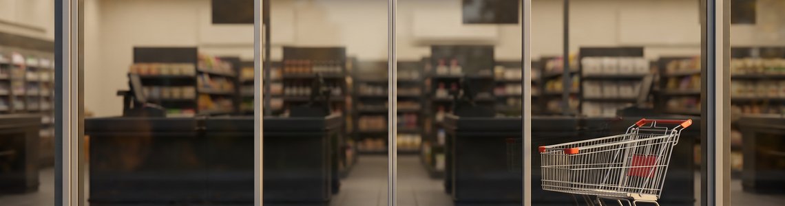 Geschlossene Glasschiebetür eines Supermarkts am Feiertagsmorgen mit leerem Einkaufswagen davor