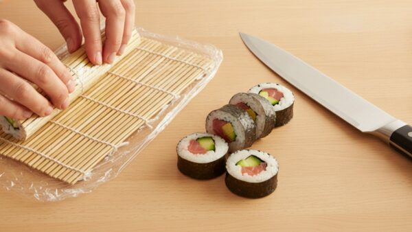 Sushi-Rolle wird auf einer mit Folie bezogenen Bambusmatte geformt und geschnitten