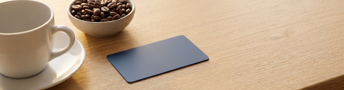 Kaffeetasse, Kaffeebohnen und unbedruckte Kundenkarte auf heller Holztheke
